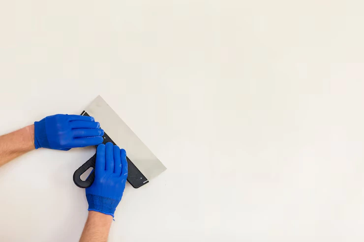 Hands holding a plastering trowel against a smooth wall, illustrating wall finishing work like plastering or rendering.
