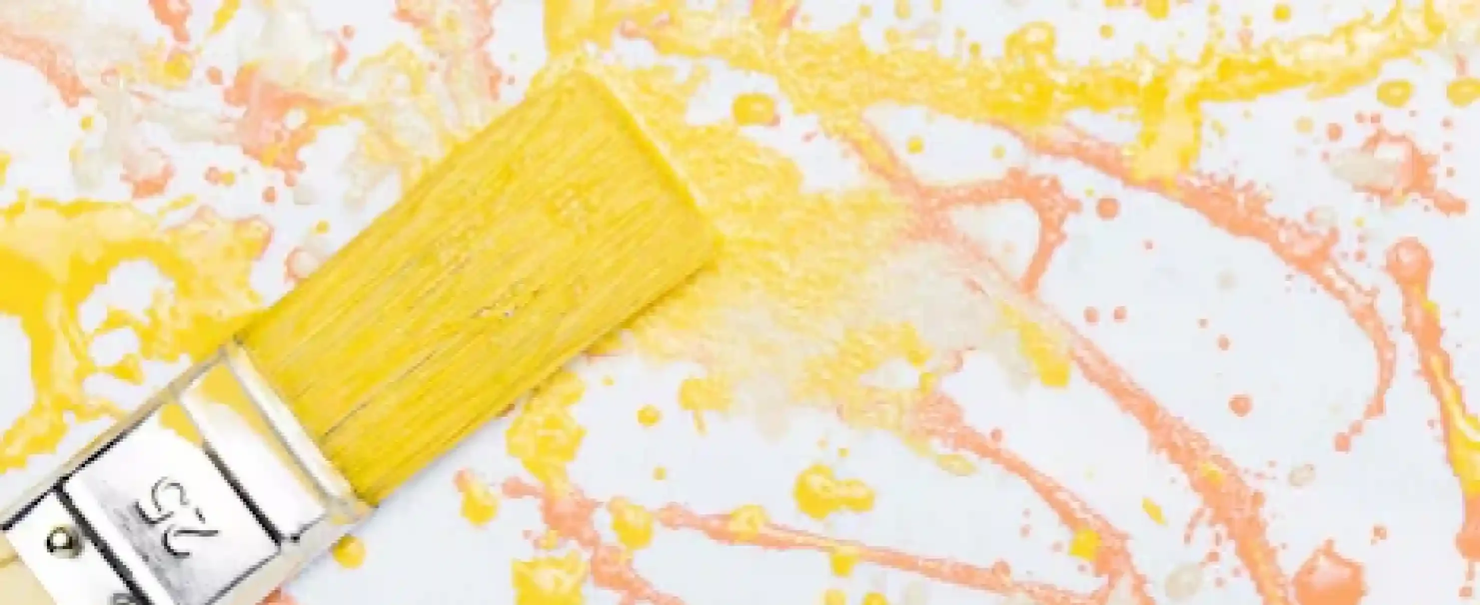 Yellow paintbrush with decorative orange and yellow paint splashes, representing creative decorative painting techniques by Pino Construction.